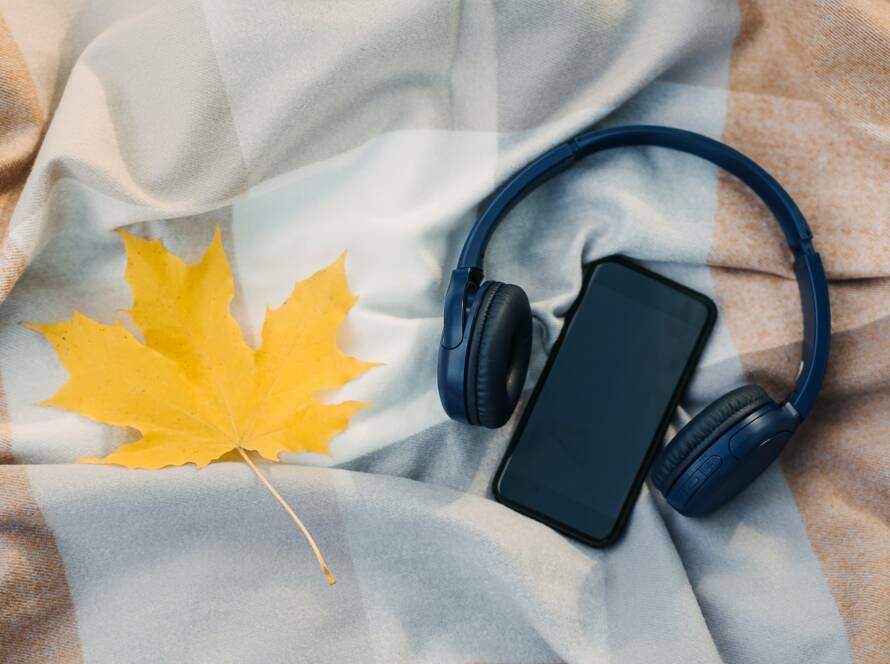 Smartphone mockup, headphones, yellow maple leaf on blanket in autumn park background. Audio